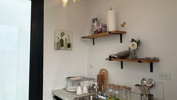 Una cocina moderna con encimera de mármol, pileta de acero inoxidable, armarios de madera y estufa negra. Hay lámparas colgantes y estantes sobre la encimera.