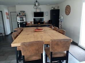 Une cuisine moderne avec une table à manger en bois, six chaises, un téléviseur et une horloge au mur.