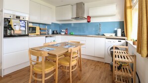 A compact kitchen with white cabinets, a wooden dining table with four chairs, a washing machine, and a drying rack. - 31 Seaward Crest (Norwich)