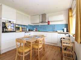 Cocina compacta con armarios blancos, una mesa de comedor de madera con cuatro sillas, lavadora y tendedero.