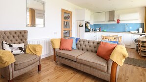 A living room with a sofa and armchairs, a kitchen in the background, and a mirror on the wall. - 31 Seaward Crest (Norwich)