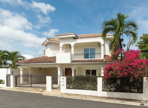 A two-story house with a tiled roof, a balcony, and a gated entrance.