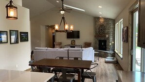 A modern kitchen with a dining area, stone fireplace, and large windows. - Explore Natures Beauty and Stay at Home in the Heart of Oregon's Wonderland (Bend)