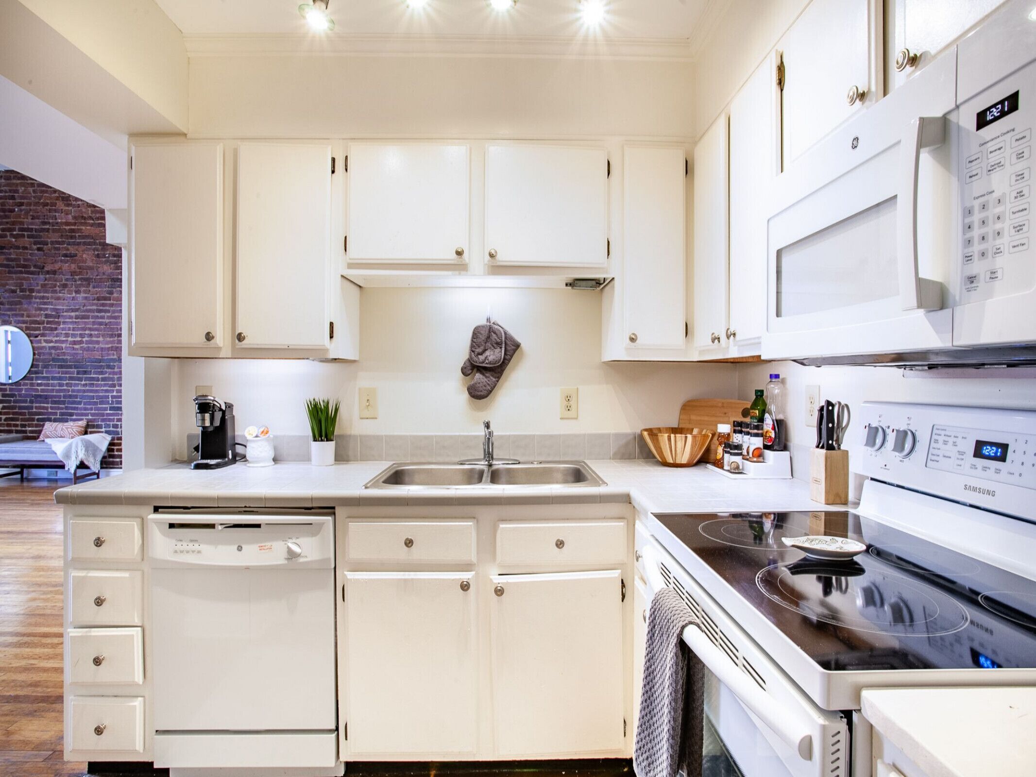 A modern kitchen with white cabinetry, a built-in dishwasher, a stainless steel sink, a microwave, and a Samsung stove.