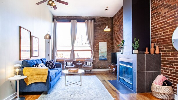 Un salon avec un canapé bleu, une table basse, une cheminée et un mur en briques.