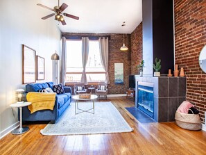 A living room with a blue sofa, a coffee table, a fireplace, and a brick wall. - Spacious Old City Loft (Knoxville)