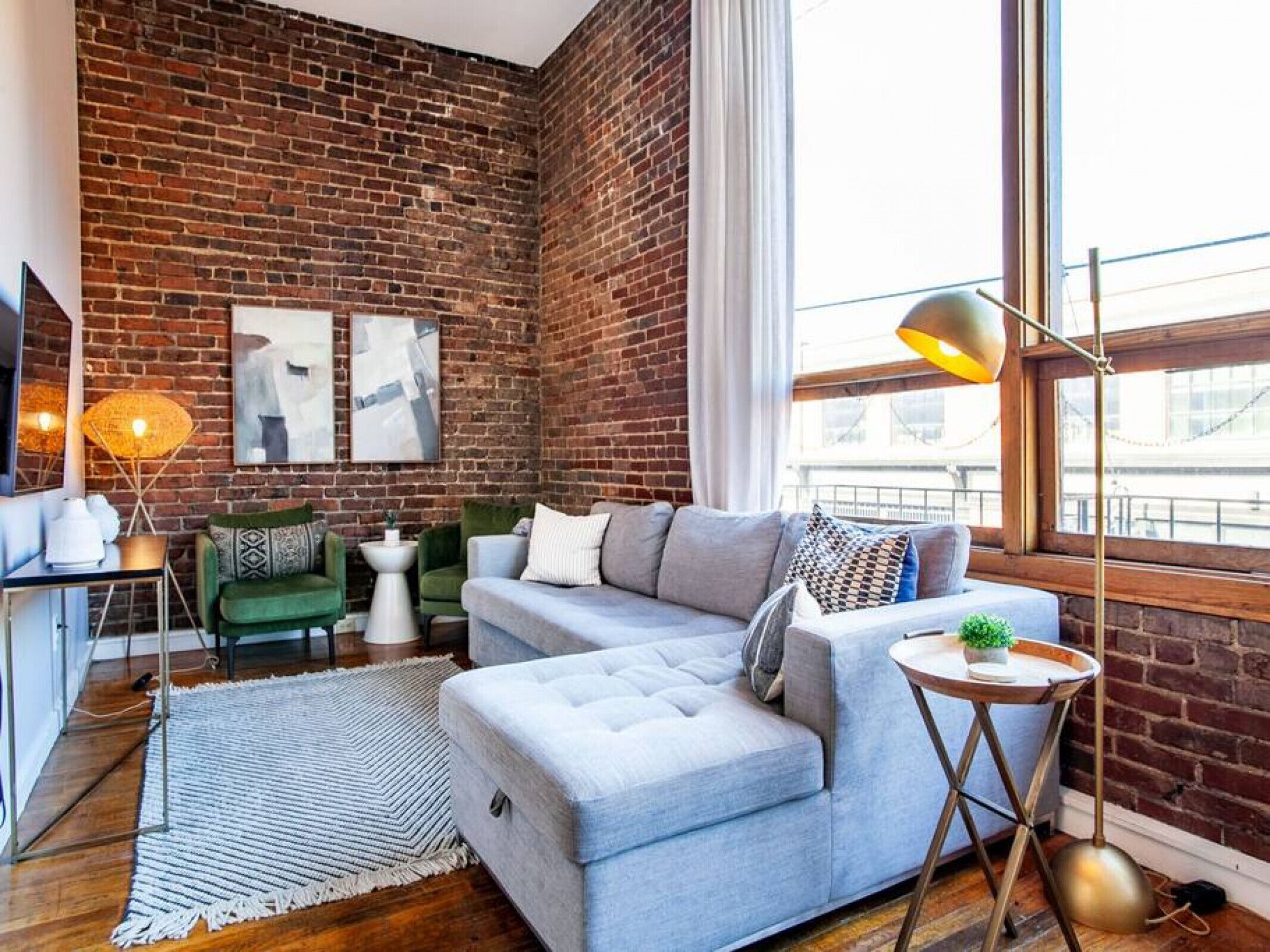 Un salon moderne avec un mur en briques, un canapé gris, une petite table ronde et un lampadaire.