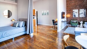 A modern apartment with a wooden floor, a grey sofa, a dining area with a table and chairs, and a brick wall. - Modern Old City Loft - Downtown Knoxville (Knoxville)