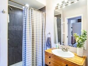 A modern bathroom with a shower, a wooden vanity with a sink, a mirror, and a potted plant. - Modern Old City Loft - Downtown Knoxville (Knoxville)