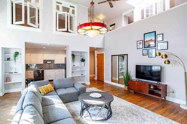 A spacious living area with a grey sectional sofa, a round coffee table, and a television on a wooden cabinet.