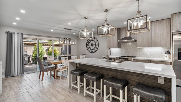 Une cuisine moderne dotée d’un grand îlot central, de tabourets de bar, de luminaires suspendus et d’une horloge murale.