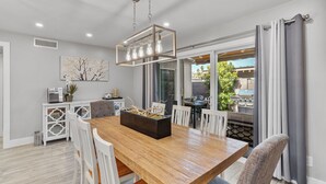 Un espace repas comprenant une table en bois, des chaises blanches, une décoration centrale noire et un luminaire suspendu.