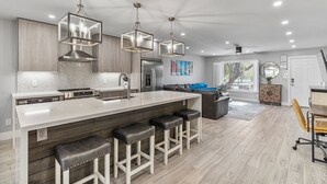 Une cuisine moderne dotée d’un grand îlot central, de tabourets de bar et de luminaires suspendus.