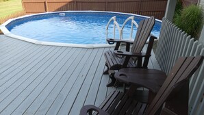 En træterrasse med swimmingpool, to træstole og et lille bord.