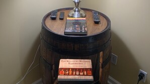 Et rundt træbord med en metlampe, to fjernbetjeninger og en bog med titlen "The Kentucky Bourbon Experience".