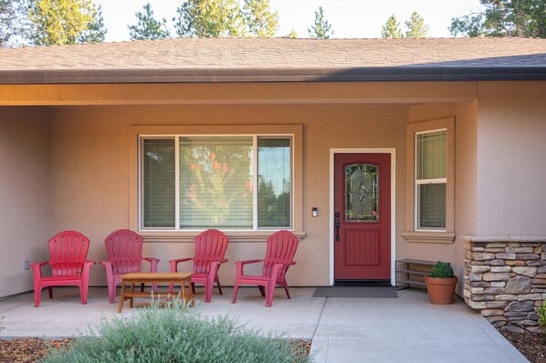 A house with a red door, a large window, and a patio with four red chairs and a table.