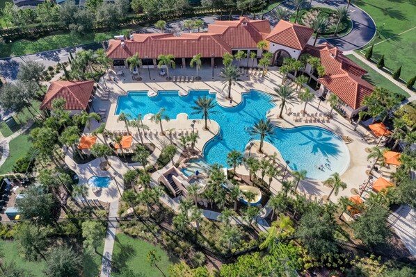 An aerial view of a resort with multiple swimming pools, palm trees, and a large building with a red-tiled roof.