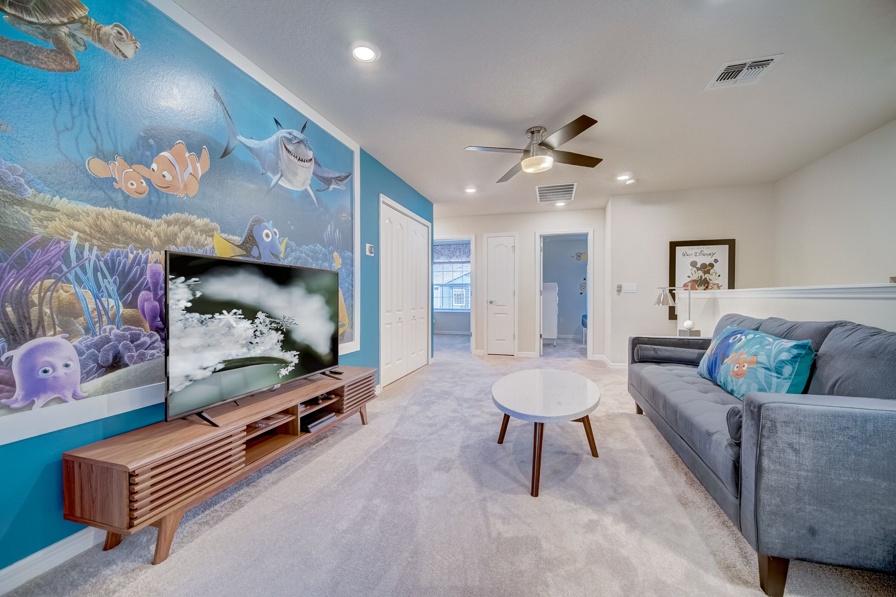 A living room with a large TV, a ceiling fan, and a mural of sea creatures.