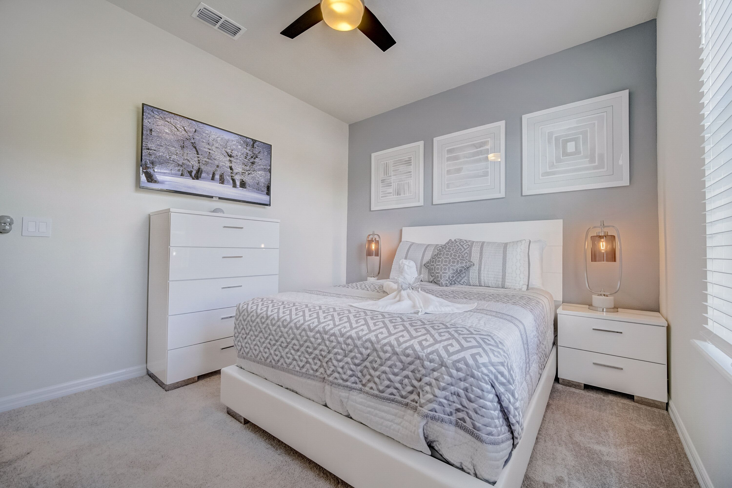 Une chambre à coucher comprenant un lit, une commode, une table de chevet et un ventilateur de plafond.