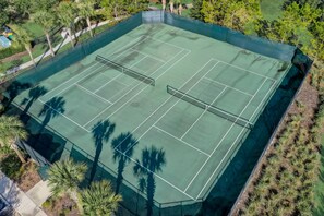 An aerial view of a tennis court surrounded by palm trees and greenery.