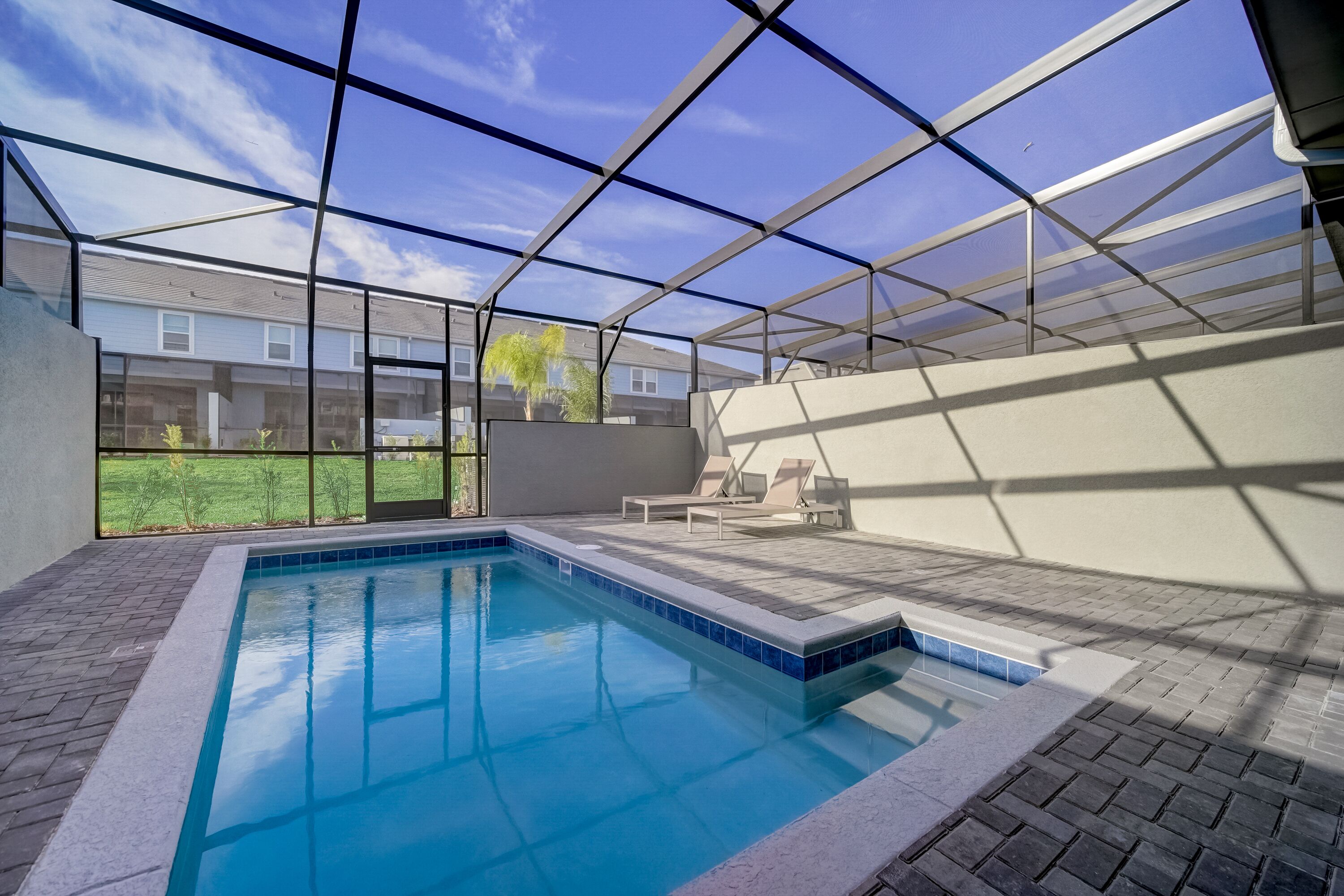 Una piscina interior con paredes de vidrio transparente, piso de baldosas y vistas a edificios cercanos.