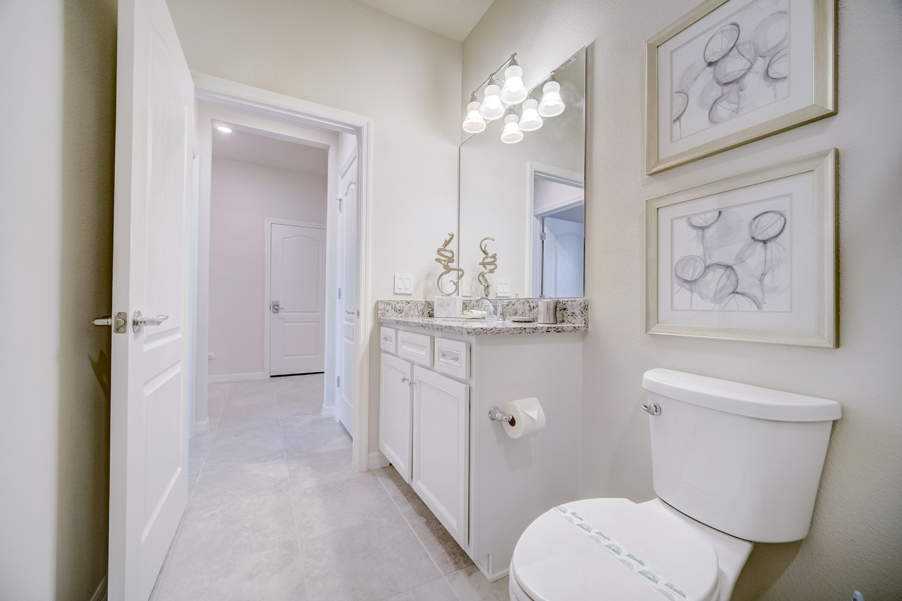 Une salle de bain comprenant des toilettes, un lavabo avec un plan de travail, un miroir et des œuvres d’art encadrées accrochées au mur.