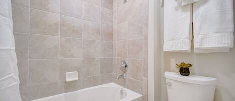 A bathroom with a bathtub, toilet, and a towel rack with towels.