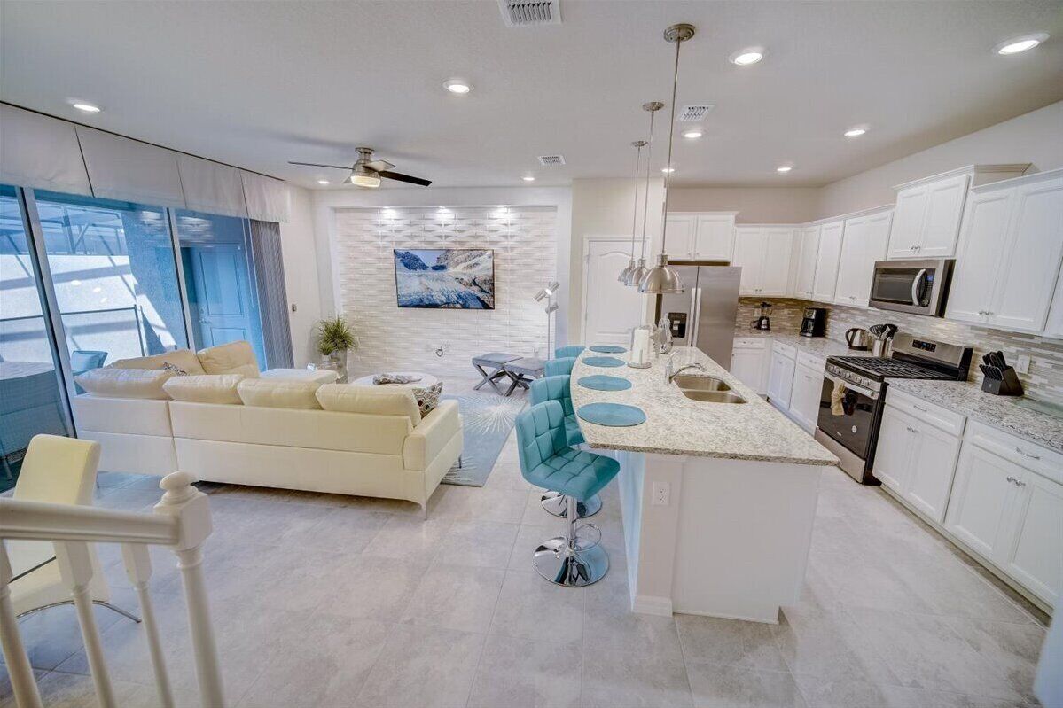 A modern kitchen with white cabinets, a central island, and a dining area with a white sofa and teal chairs.