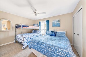 A bedroom with two beds, a ceiling fan, a window with curtains, and a door.