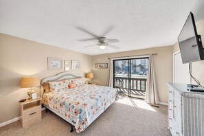 A bedroom with a bed, nightstands, a dresser, a ceiling fan, and a balcony with a view of the city.