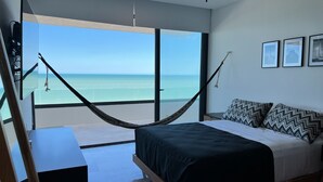 A bedroom with a large window, a hammock, a bed with patterned pillows, and framed pictures on the wall. - Luxury beachfront condo w/private jacuzzi  (Telchac Puerto)