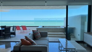 A modern living room with a view of the ocean, a sofa with cushions, a dining table, and a ceiling fan. - Luxury beachfront condo w/private jacuzzi  (Telchac Puerto)