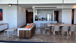A modern living room with a sofa, coffee table, and dining area with chairs. - Luxury beachfront condo w/private jacuzzi  (Telchac Puerto)