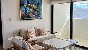 A modern living room with a sofa, two wooden chairs, a small round table, and a large painting of a sea turtle. - Luxury beachfront condo w/private jacuzzi  (Telchac Puerto)