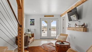 A spacious living room with a large window, a wooden staircase, a television mounted on the wall, and a drum.