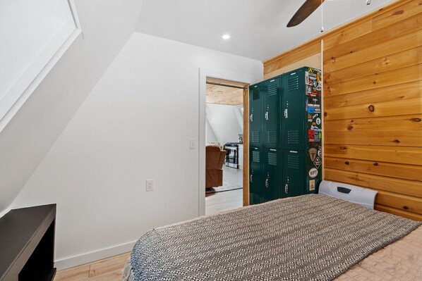 A bedroom with a sloped ceiling, a bed with patterned bedding, a wooden wall panel, and a door leading to another room.