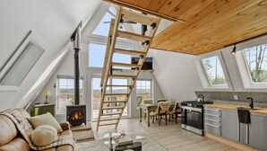 A loft-style living room with a wooden ladder, a fireplace, a sofa, and a kitchen area with a stove and cabinets. - EPIC VIEWS - Pond - Crooked River 14 ACRES - SECLUDED (Harrison)