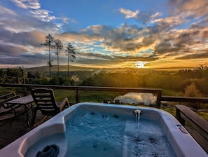 A hot tub on a deck with a view of a sunset over a valley.
