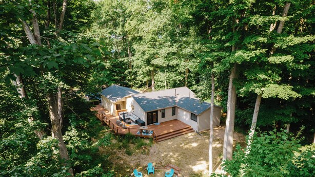 Une maison dotée d’une terrasse, d’un espace salon extérieur et d’un foyer entouré d’arbres.