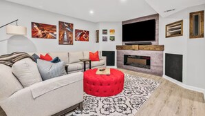 Un salon moderne avec un canapé, un pouf, une cheminée et des œuvres d’art accrochées aux murs.