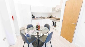 A compact kitchen with white cabinets, a microwave, and a coffee maker. There is a small dining area with a glass table and four chairs. - Modern Apartment in Salford, Manchester, UK (Salford)