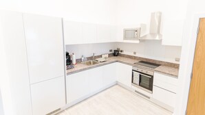 A modern kitchen with white cabinets, a stainless steel sink, a microwave, and an oven. - Modern Apartment in Salford, Manchester, UK (Salford)