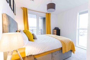 A modern bedroom with a bed, a bedside table, a lamp, and a window with curtains. - Modern Apartment in Salford, Manchester, UK (Salford)