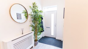 A hallway with a radiator, a mirror, a potted plant, and a door. - Modern Apartment in Salford, Manchester, UK (Salford)
