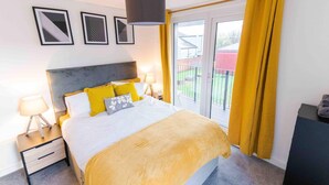 A bedroom with a bed, bedside lamps, a nightstand, a window with yellow curtains, and a view of the outside. - Modern Apartment in Salford, Manchester, UK (Salford)