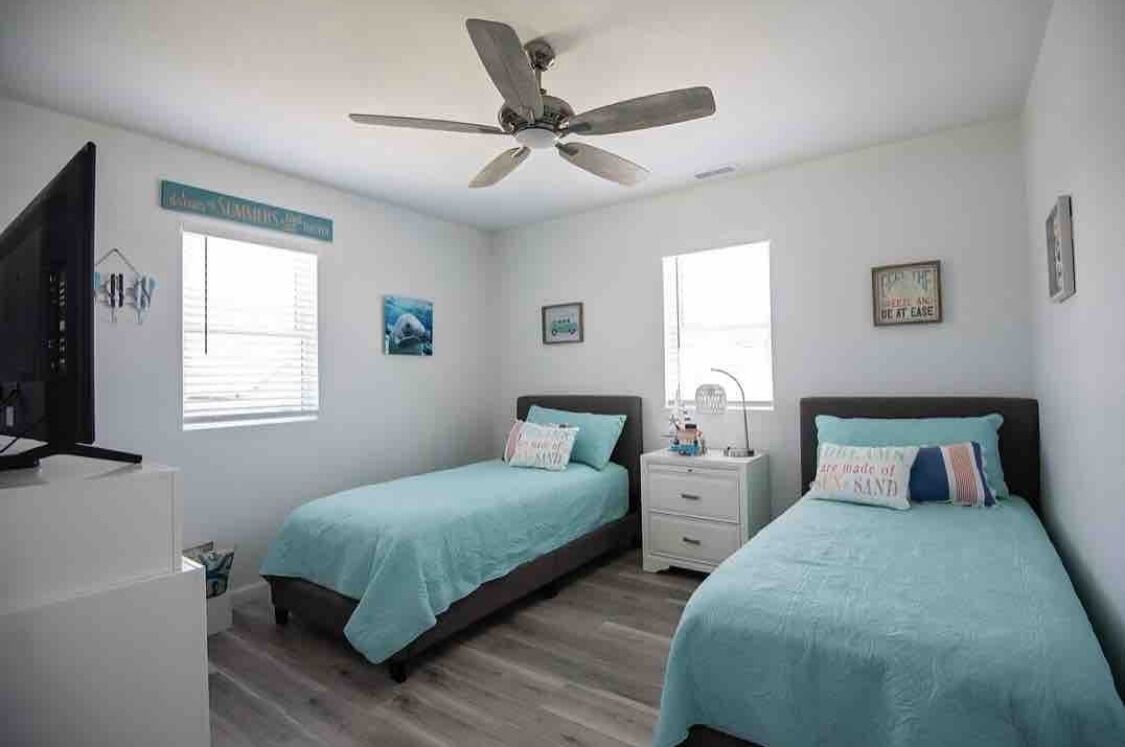 A bedroom with two beds, a ceiling fan, a TV, and a window.
