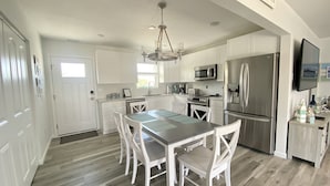 Una cocina moderna con muebles blancos, electrodomésticos de acero inoxidable y una zona de comedor con sillas y mesa blancos.