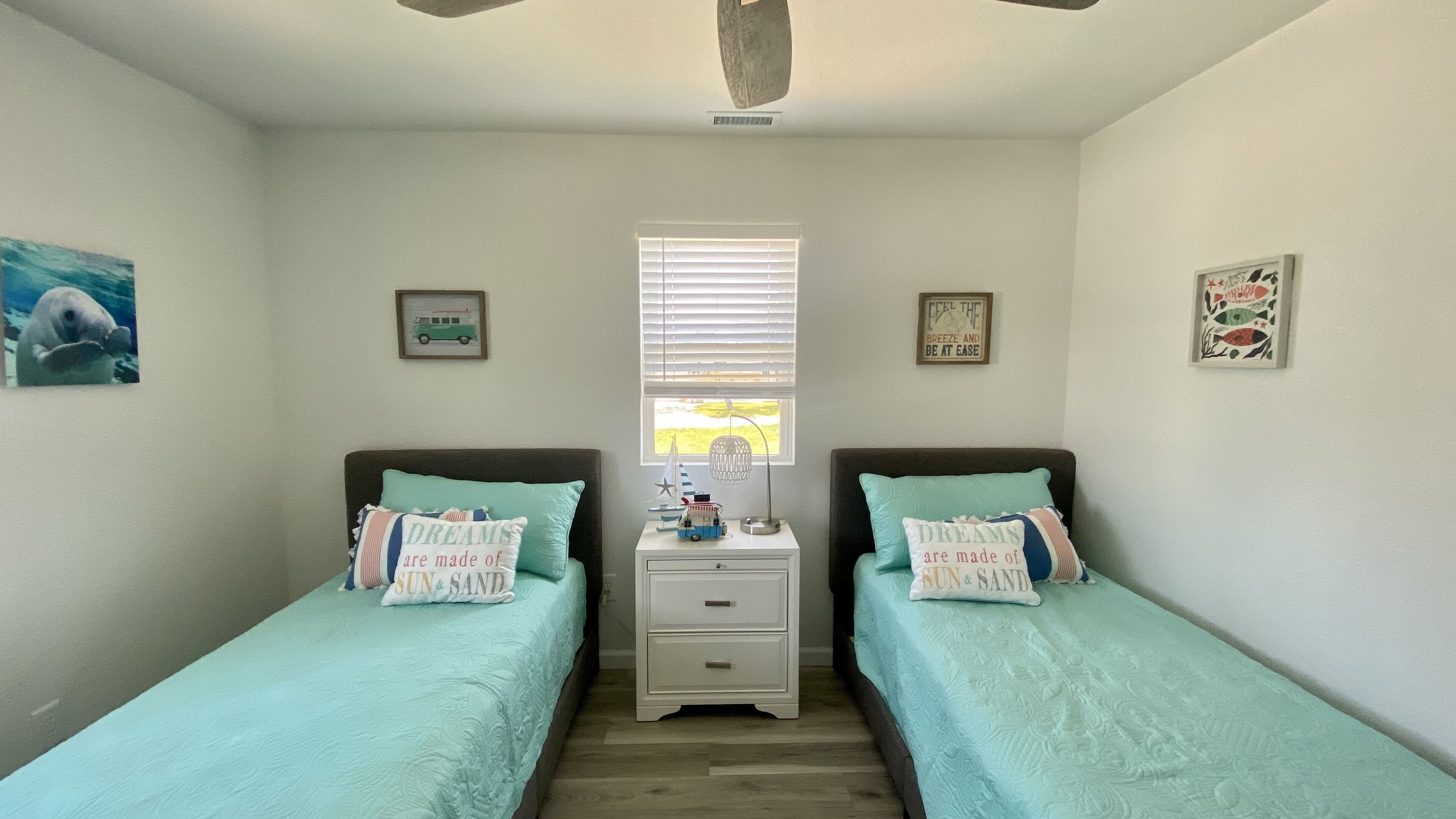 A bedroom with two single beds, a nightstand between them, and a window with blinds.