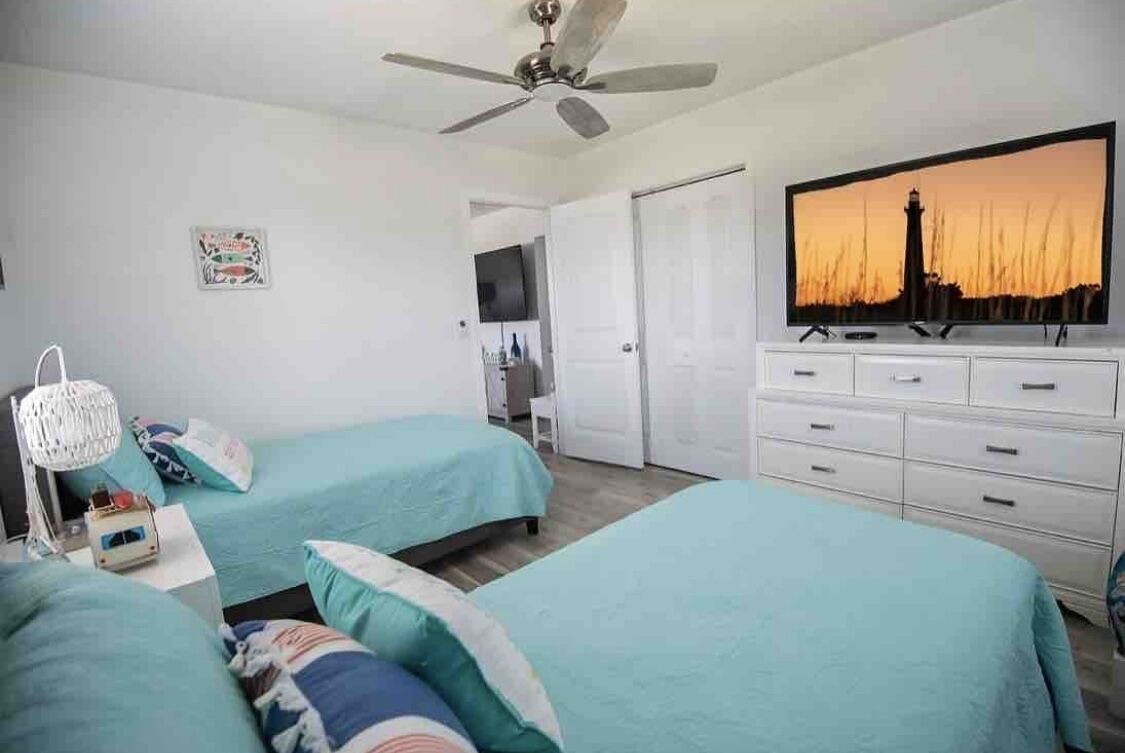 Une chambre avec deux lits, un ventilateur de plafond, une télévision et une commode.