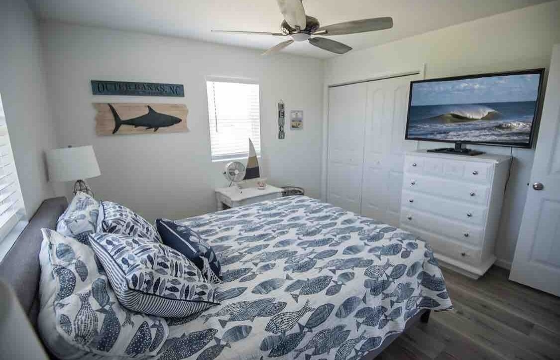 Une chambre à coucher comprenant un lit, une commode, un téléviseur, un ventilateur de plafond et une fenêtre.